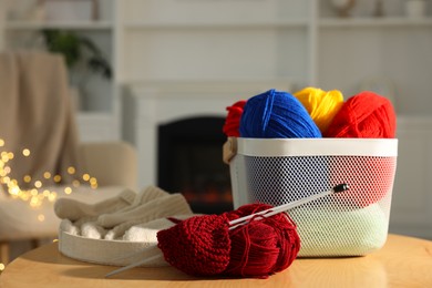 Photo of Colorful yarns, knitting needles, mittens and basket on wooden table indoors