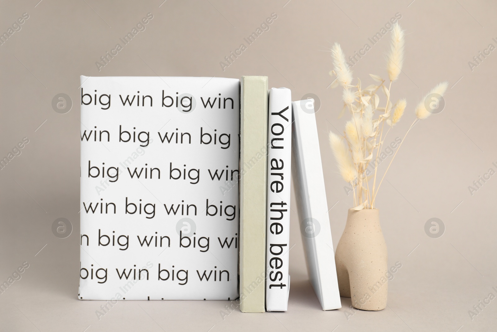 Photo of White books with phrases You are the best and Big win between ones and vase with spikelets on light grey background