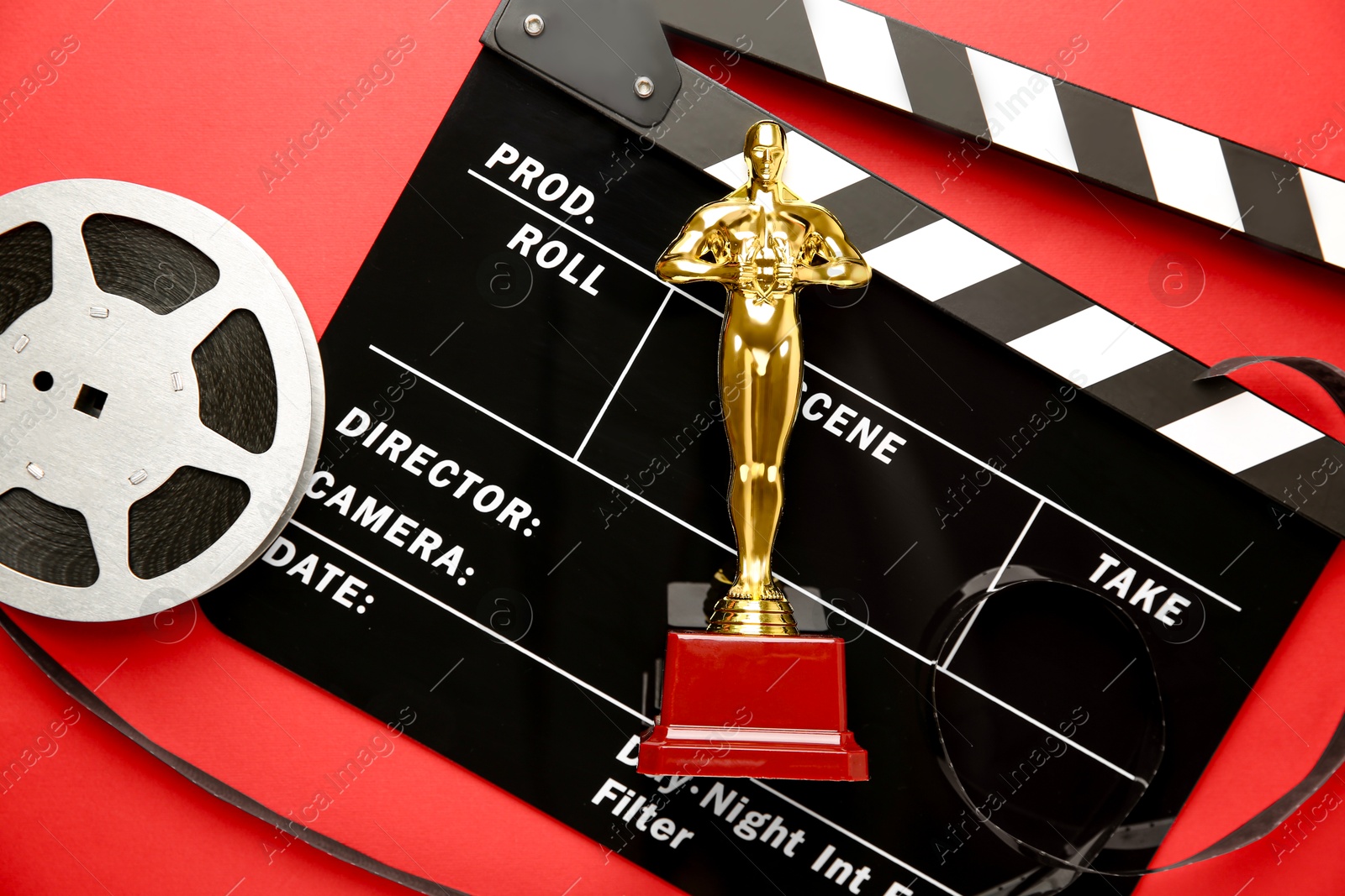 Photo of Golden trophy in shape of human figure, movie clapper and film reel on red background, top view