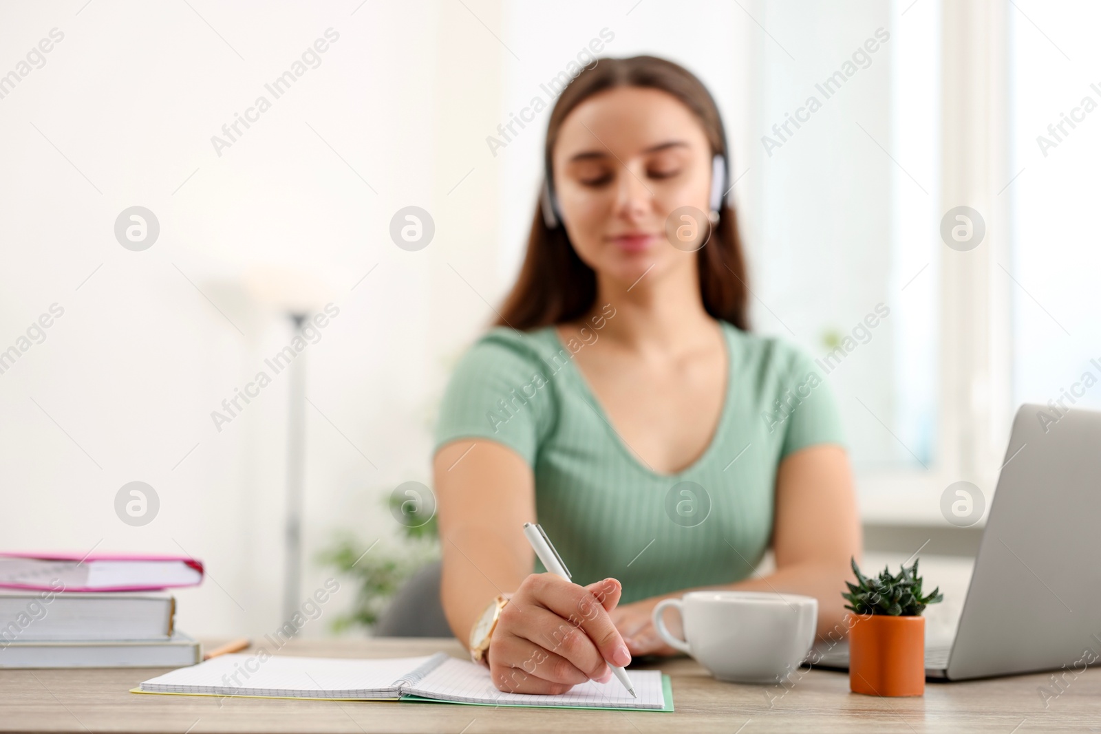 Photo of Student in headphones studying at wooden table indoors, selective focus