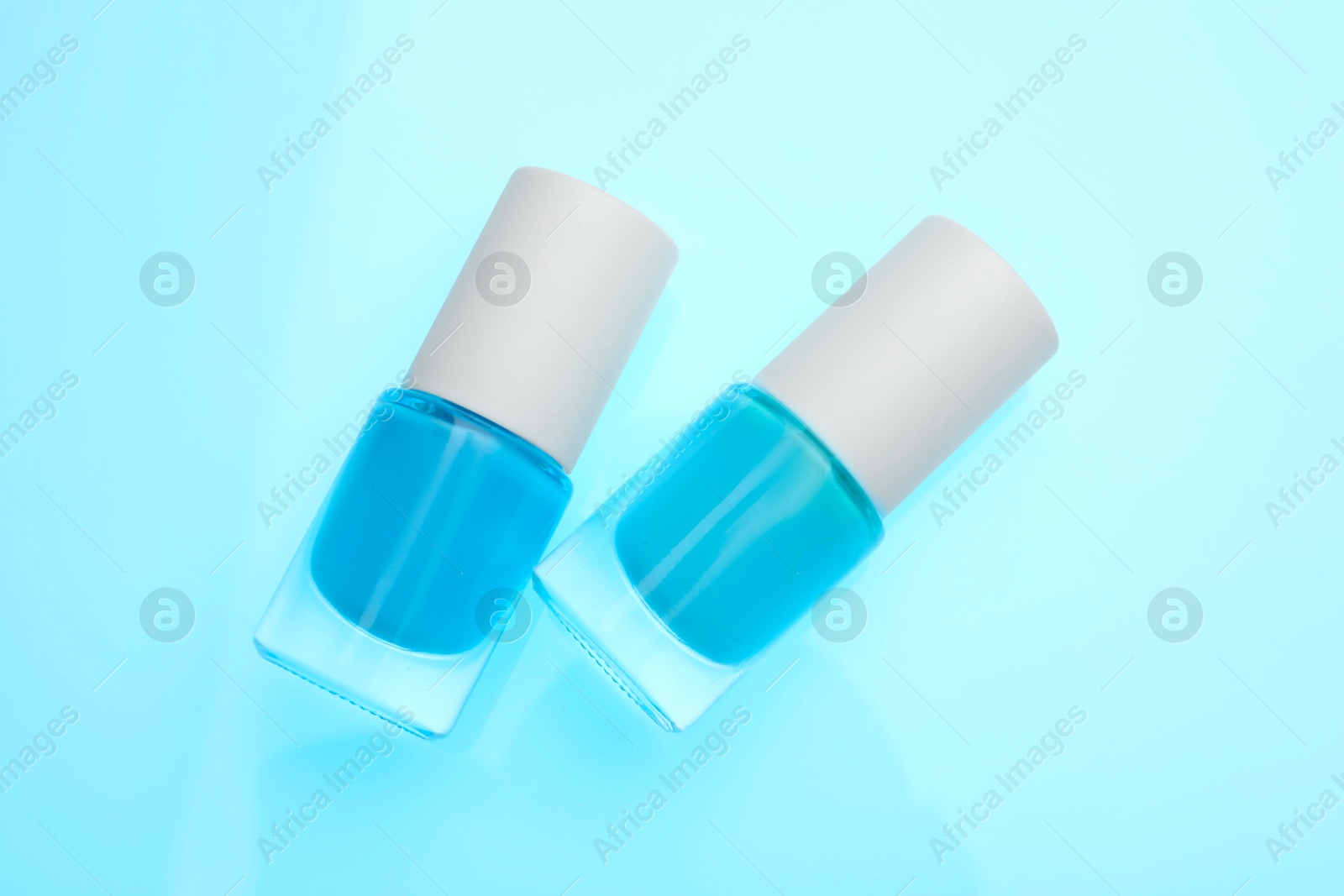 Photo of Nail polish in bottles on light blue background, top view