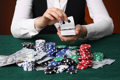 Photo of Professional croupier with chips shuffling playing cards at gambling table on color background, closeup