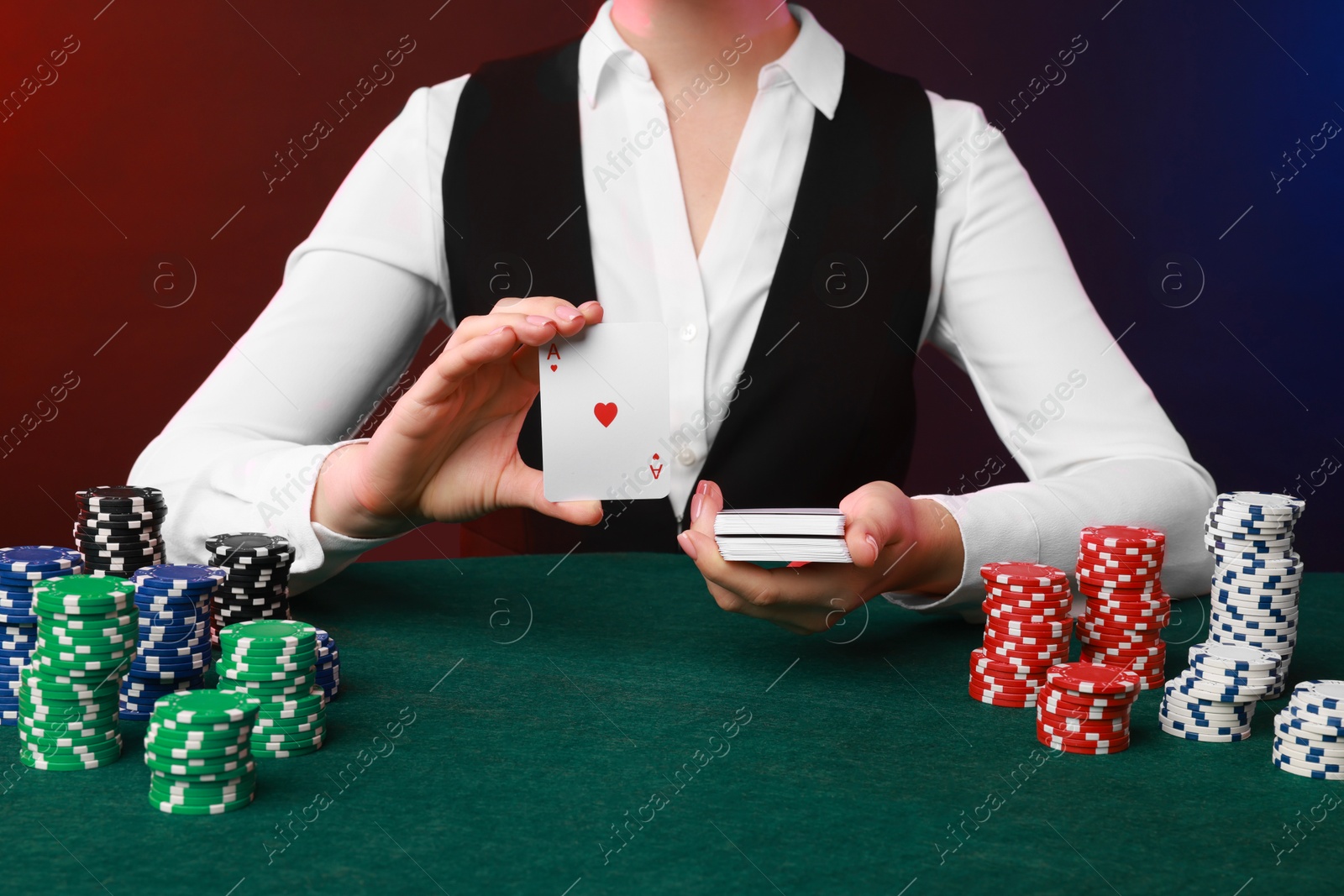 Photo of Professional croupier with casino chips and playing cards at gambling table on color background, closeup