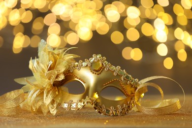 Photo of Beautiful carnival mask on golden shiny surface against blurred lights, closeup