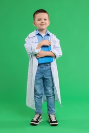 Photo of Little boy with book pretending to be doctor on green background. Dreaming of future profession