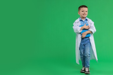 Photo of Little boy with book pretending to be doctor on green background, space for text. Dreaming of future profession