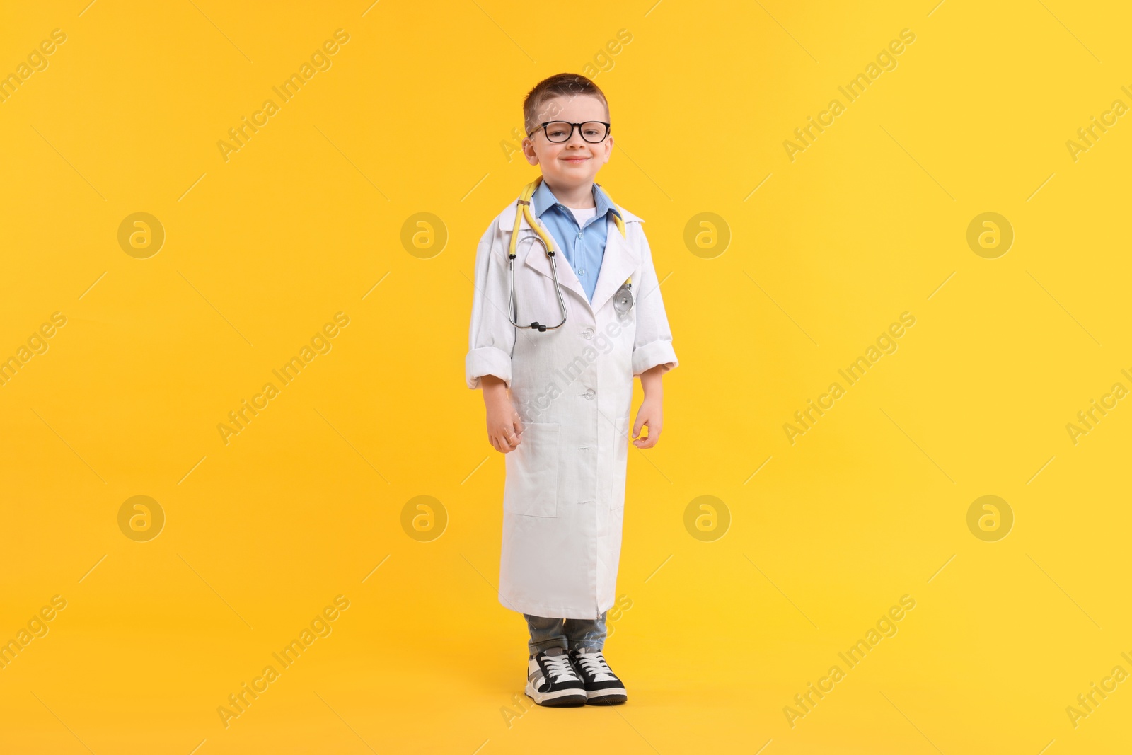 Photo of Little boy with stethoscope pretending to be doctor on yellow background, space for text. Dreaming of future profession