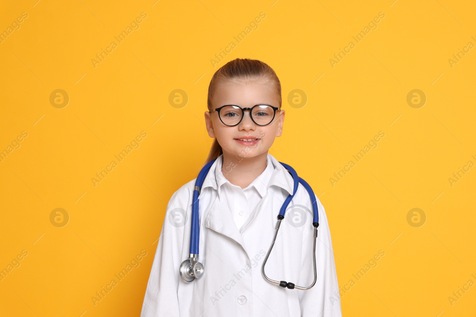 Photo of Little girl with stethoscope pretending to be doctor on orange background. Dreaming of future profession