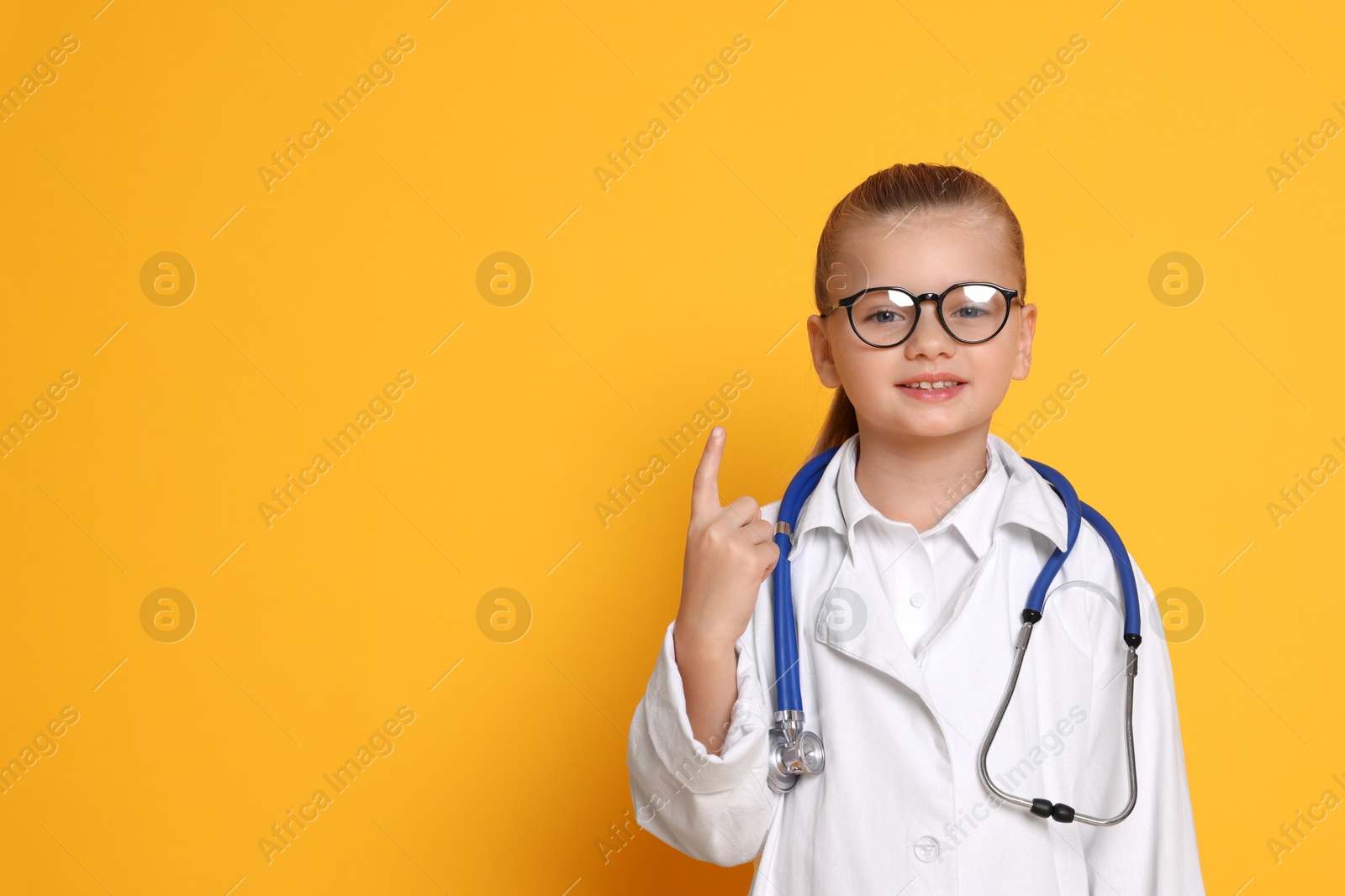 Photo of Little girl with stethoscope pretending to be doctor on orange background, space for text. Dreaming of future profession