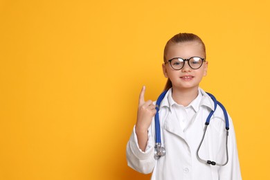 Little girl with stethoscope pretending to be doctor on orange background, space for text. Dreaming of future profession