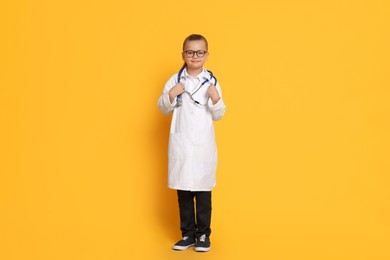 Photo of Little girl with stethoscope pretending to be doctor on orange background. Dreaming of future profession