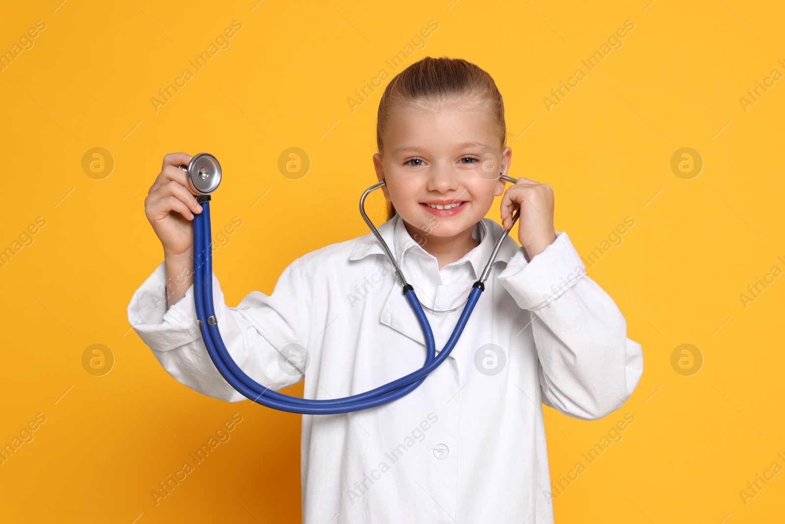 Photo of Little girl with stethoscope pretending to be doctor on orange background. Dreaming of future profession