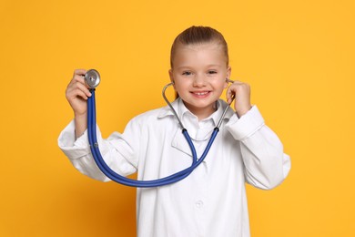 Photo of Little girl with stethoscope pretending to be doctor on orange background. Dreaming of future profession