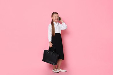 Photo of Little girl with bag talking on smartphone and pretending to be businesswoman against pink background. Dreaming of future profession