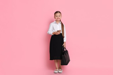 Photo of Little girl with bag and smartphone pretending to be businesswoman on pink background. Dreaming of future profession