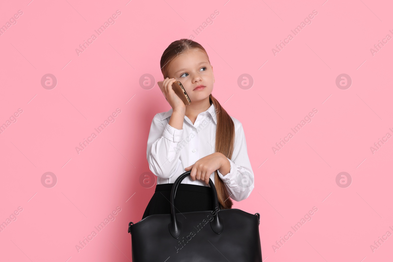 Photo of Little girl with bag talking on smartphone and pretending to be businesswoman against pink background. Dreaming of future profession