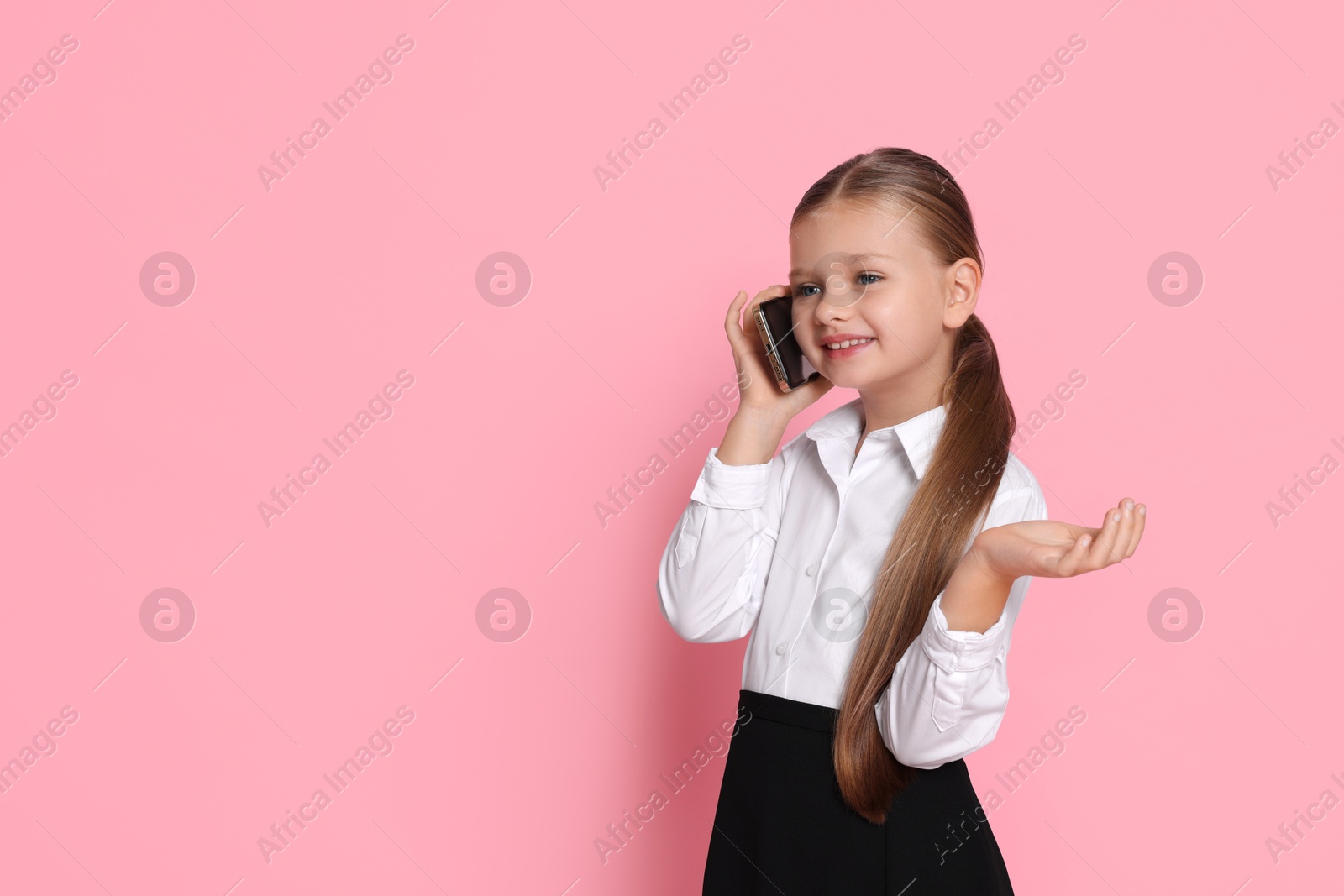 Photo of Little girl talking on smartphone and pretending to be businesswoman against pink background, space for text. Dreaming of future profession