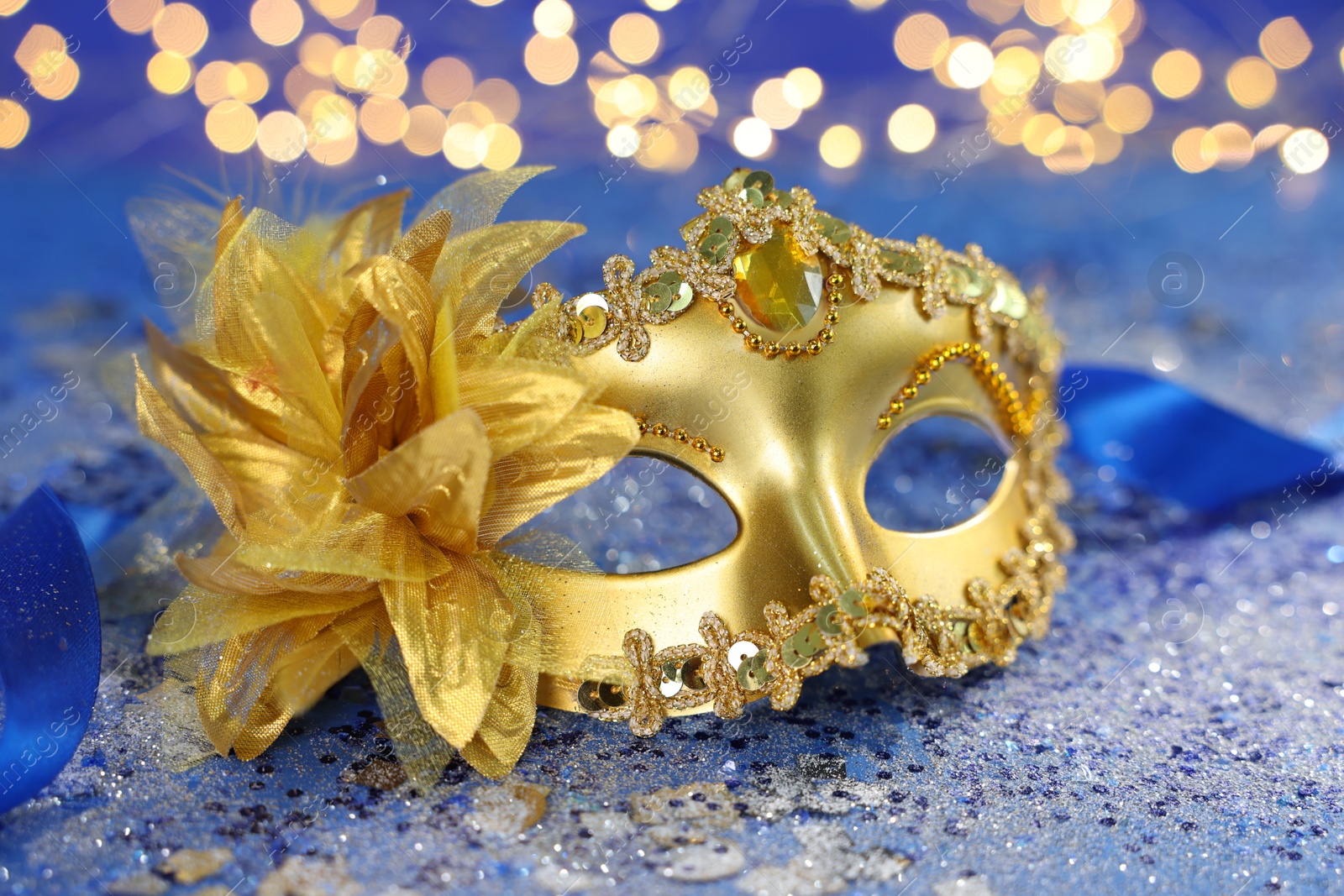 Photo of Beautiful carnival mask on blue glitter background against blurred lights, closeup. Bokeh effect