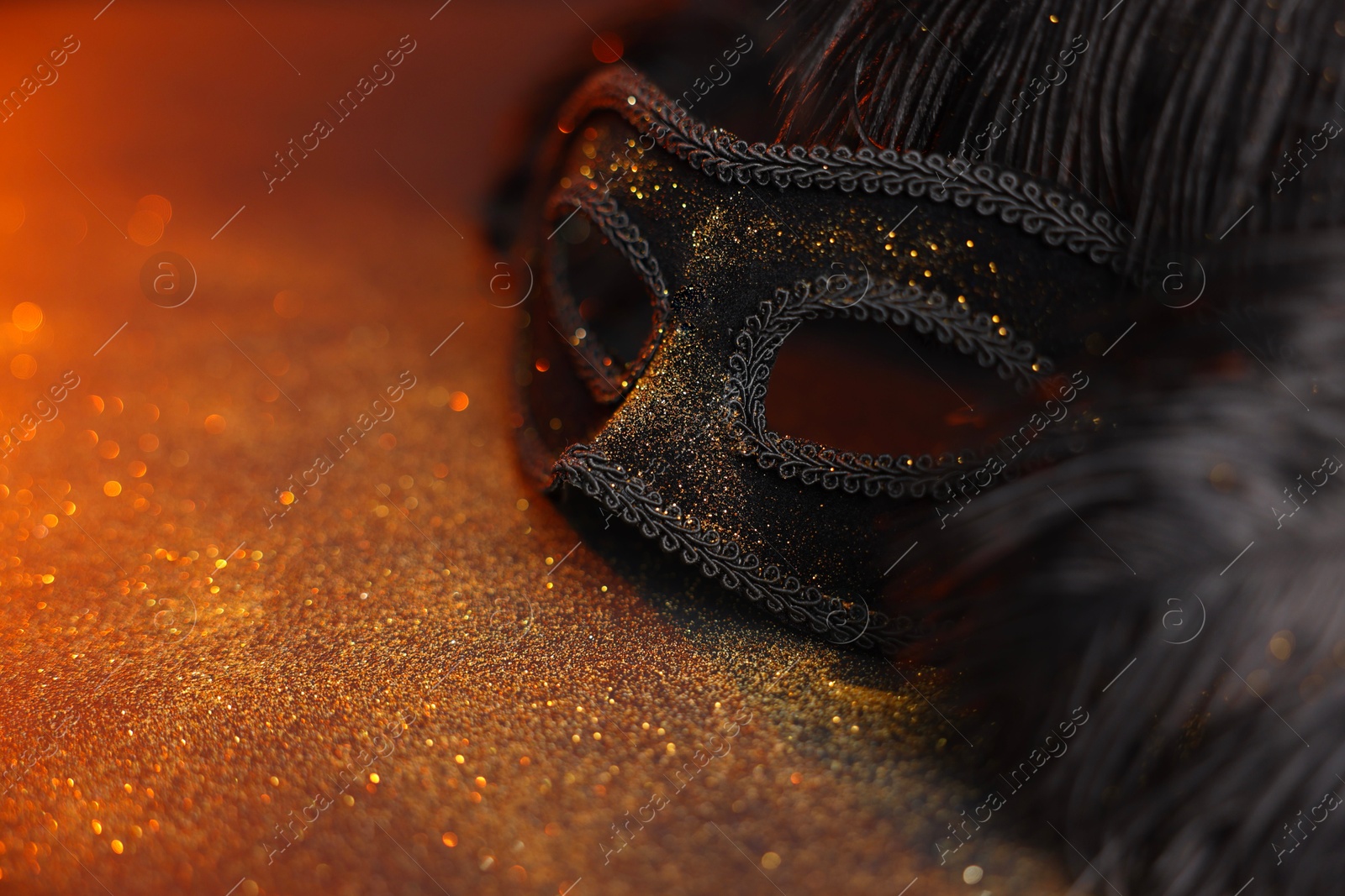 Photo of Beautiful carnival mask and black feathers on glitter background, closeup. Space for text