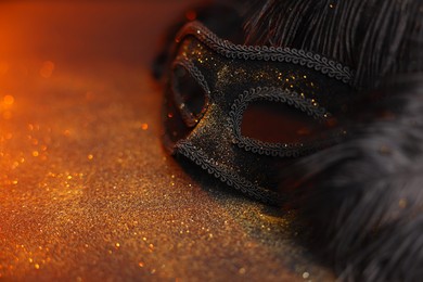 Photo of Beautiful carnival mask and black feathers on glitter background, closeup. Space for text