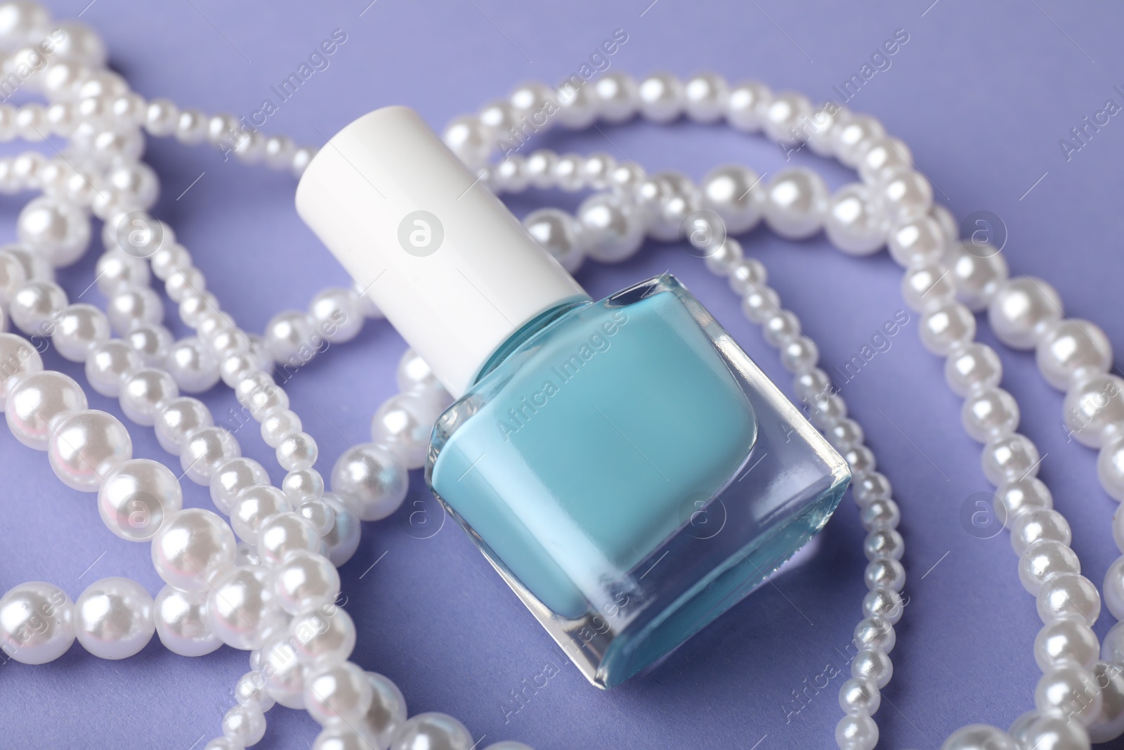 Photo of Nail polish in bottle and necklace on purple background, closeup