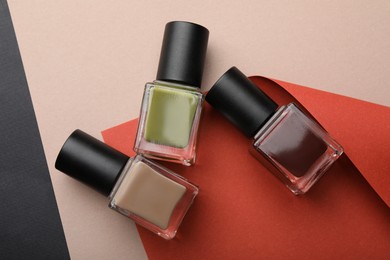 Photo of Nail polishes in bottles and color paper on beige background, flat lay