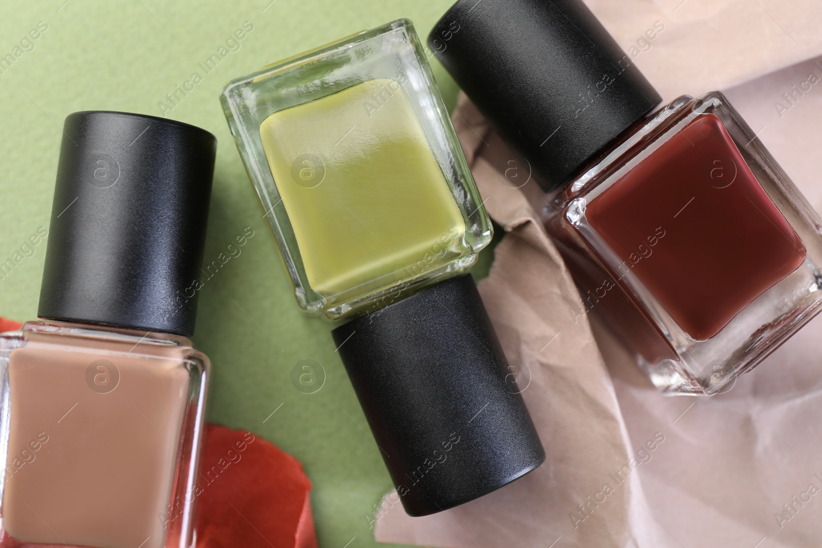 Photo of Nail polishes in bottles and craft paper on olive background, flat lay