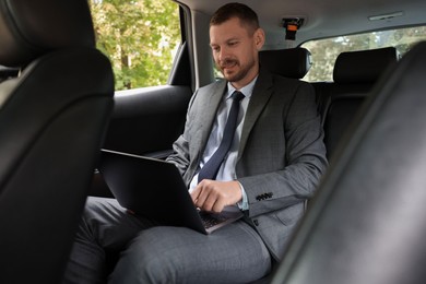 Smiling man using laptop in modern car