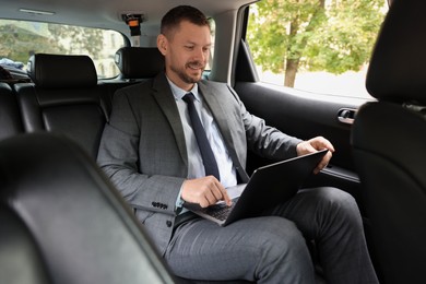 Photo of Smiling man using laptop in modern car