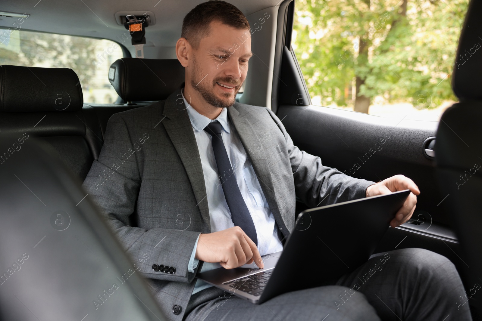 Photo of Smiling man using laptop in modern car