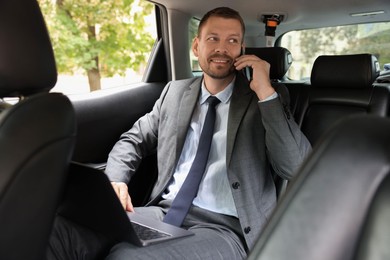 Photo of Man with laptop talking on phone in modern car