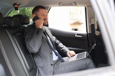 Photo of Man with laptop talking on phone in modern car