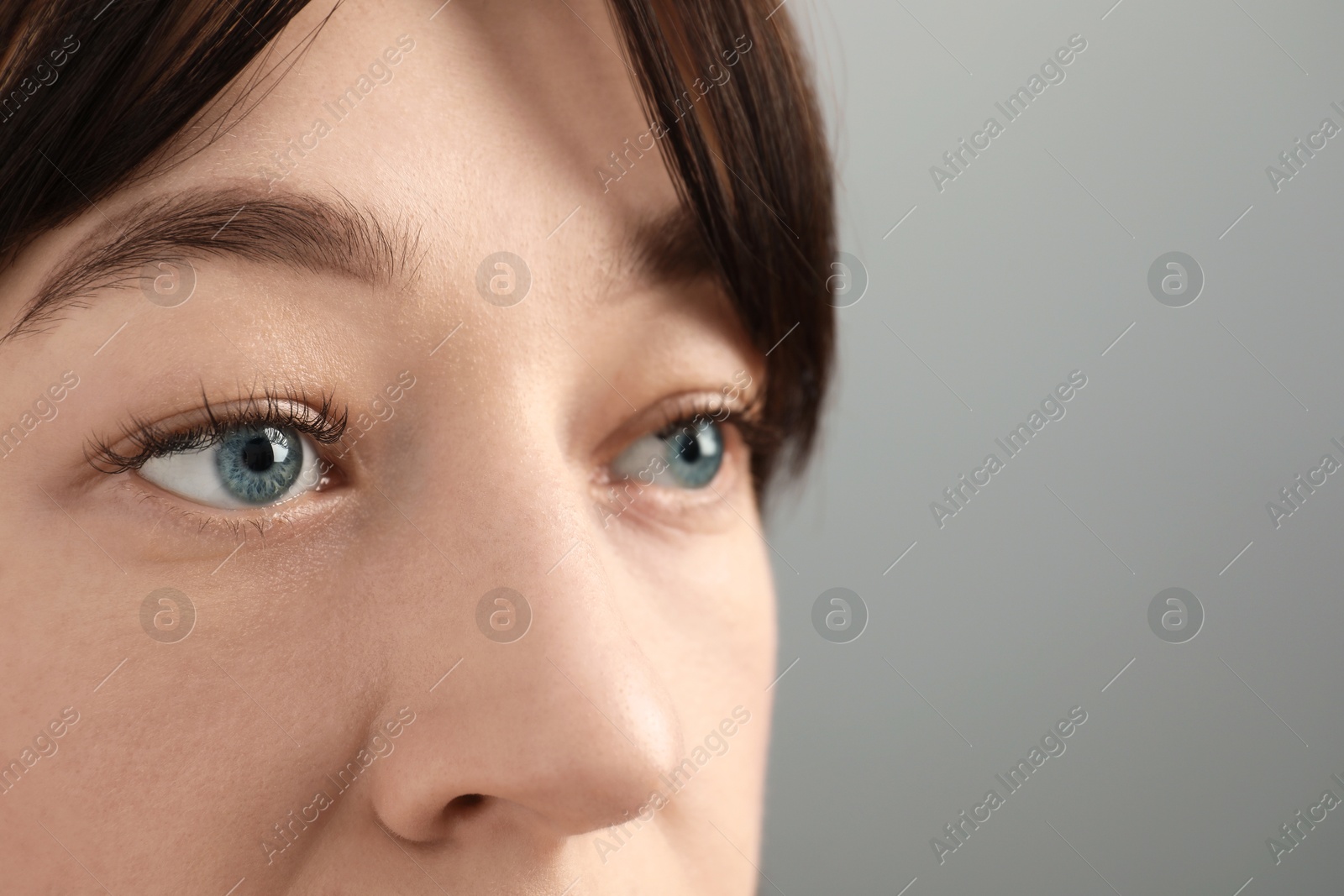 Photo of Young woman with beautiful blue eyes on grey background, closeup. Space for text