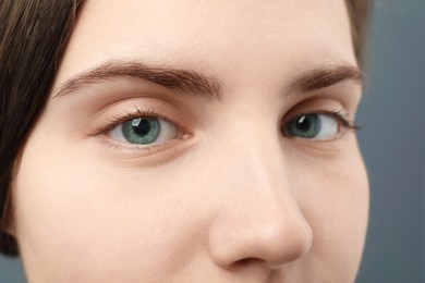 Photo of Closeup view of young woman with beautiful blue eyes on grey background