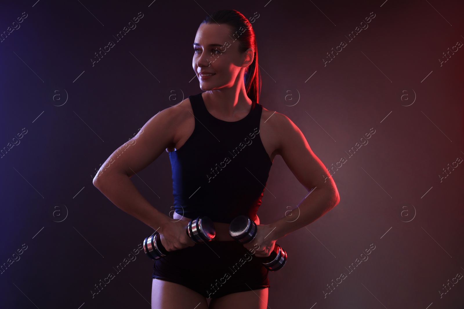 Photo of Woman exercising with dumbbells in smoke on dark background