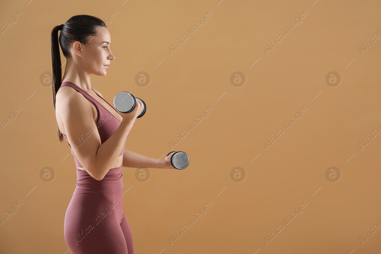 Photo of Woman exercising with dumbbells on beige background, space for text