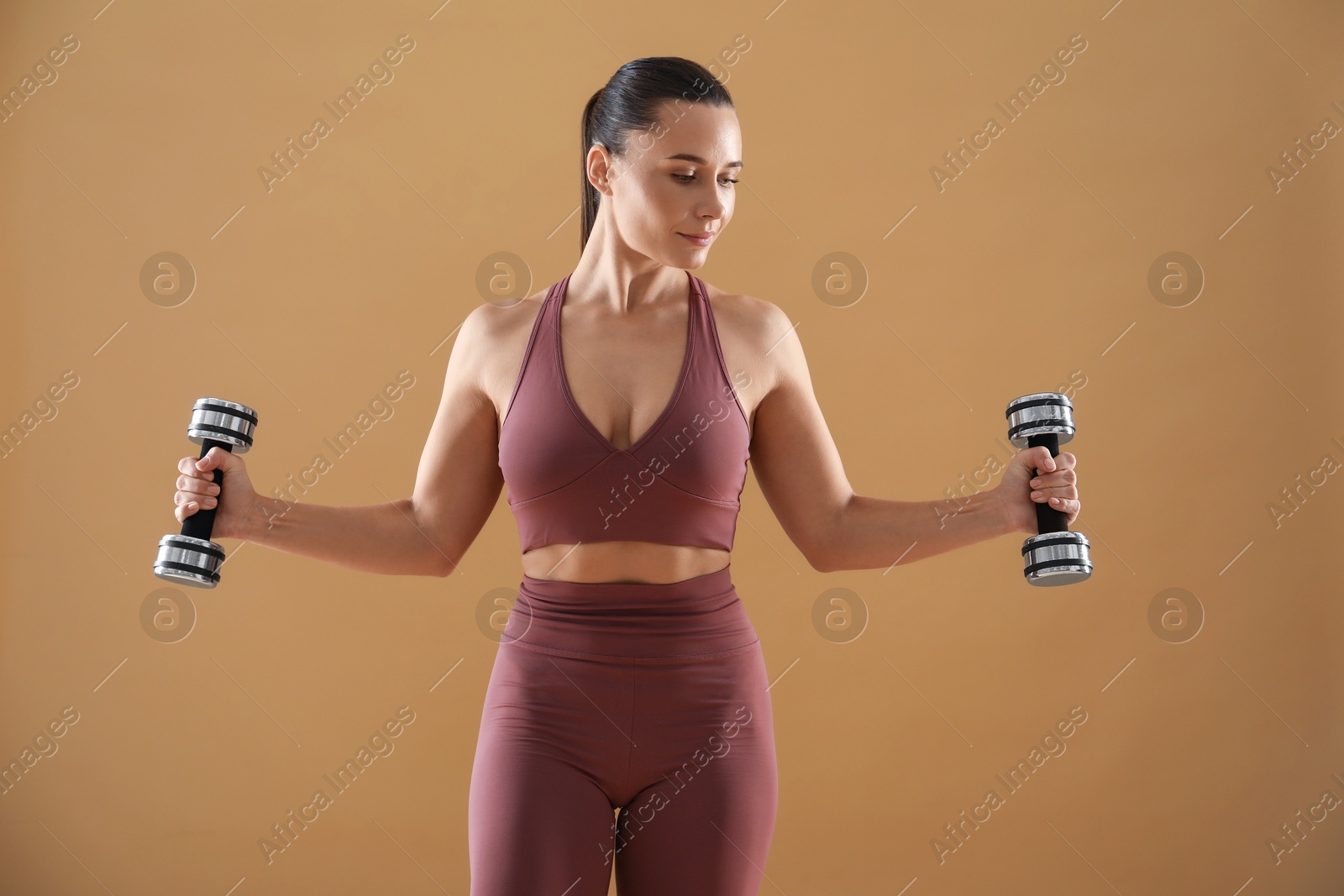 Photo of Woman exercising with dumbbells on beige background