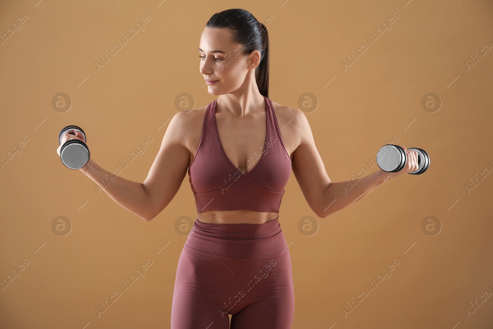 Photo of Woman exercising with dumbbells on beige background