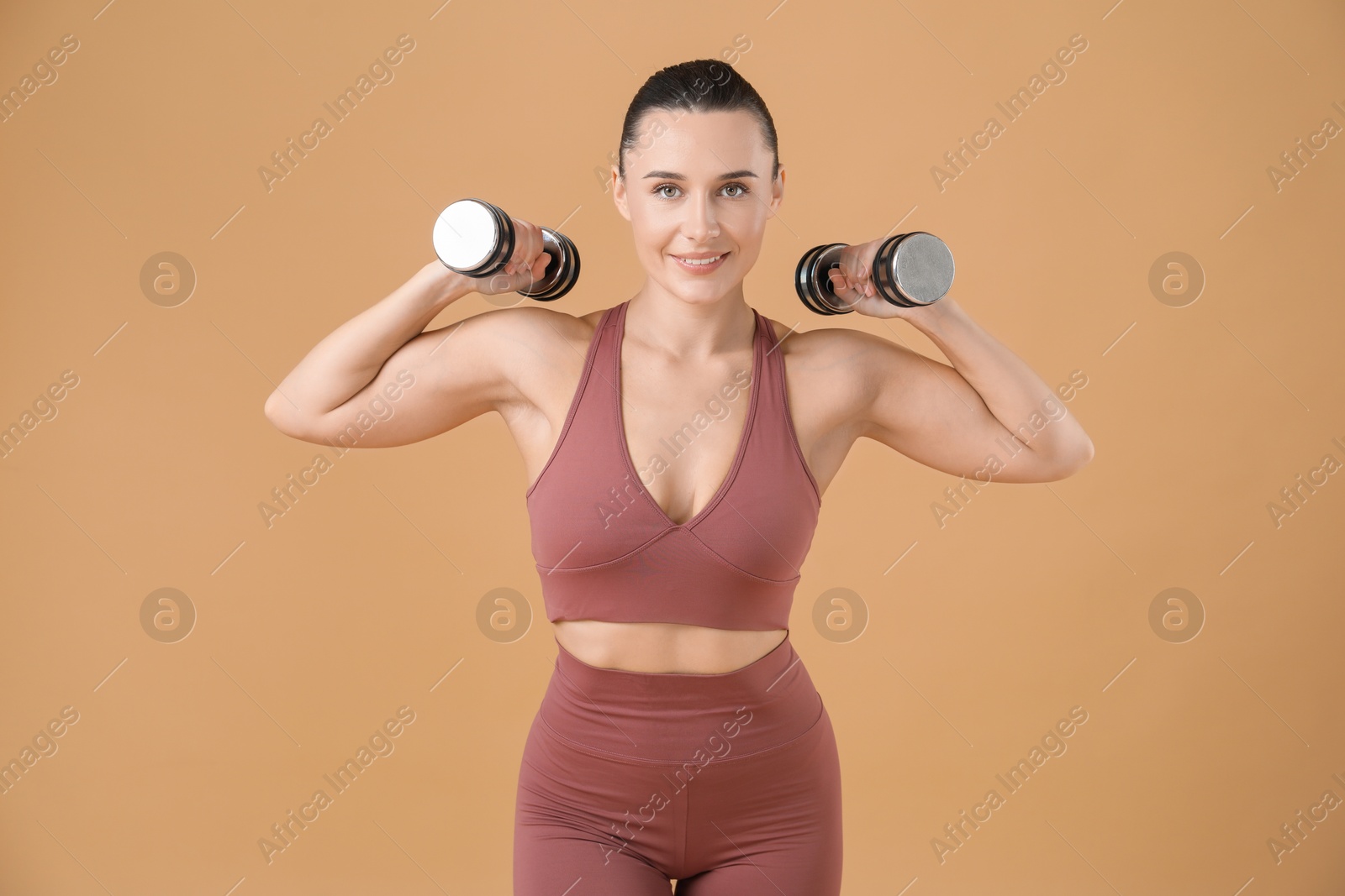 Photo of Woman exercising with dumbbells on beige background