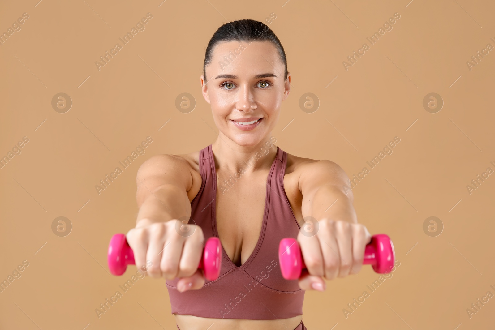 Photo of Woman exercising with dumbbells on beige background