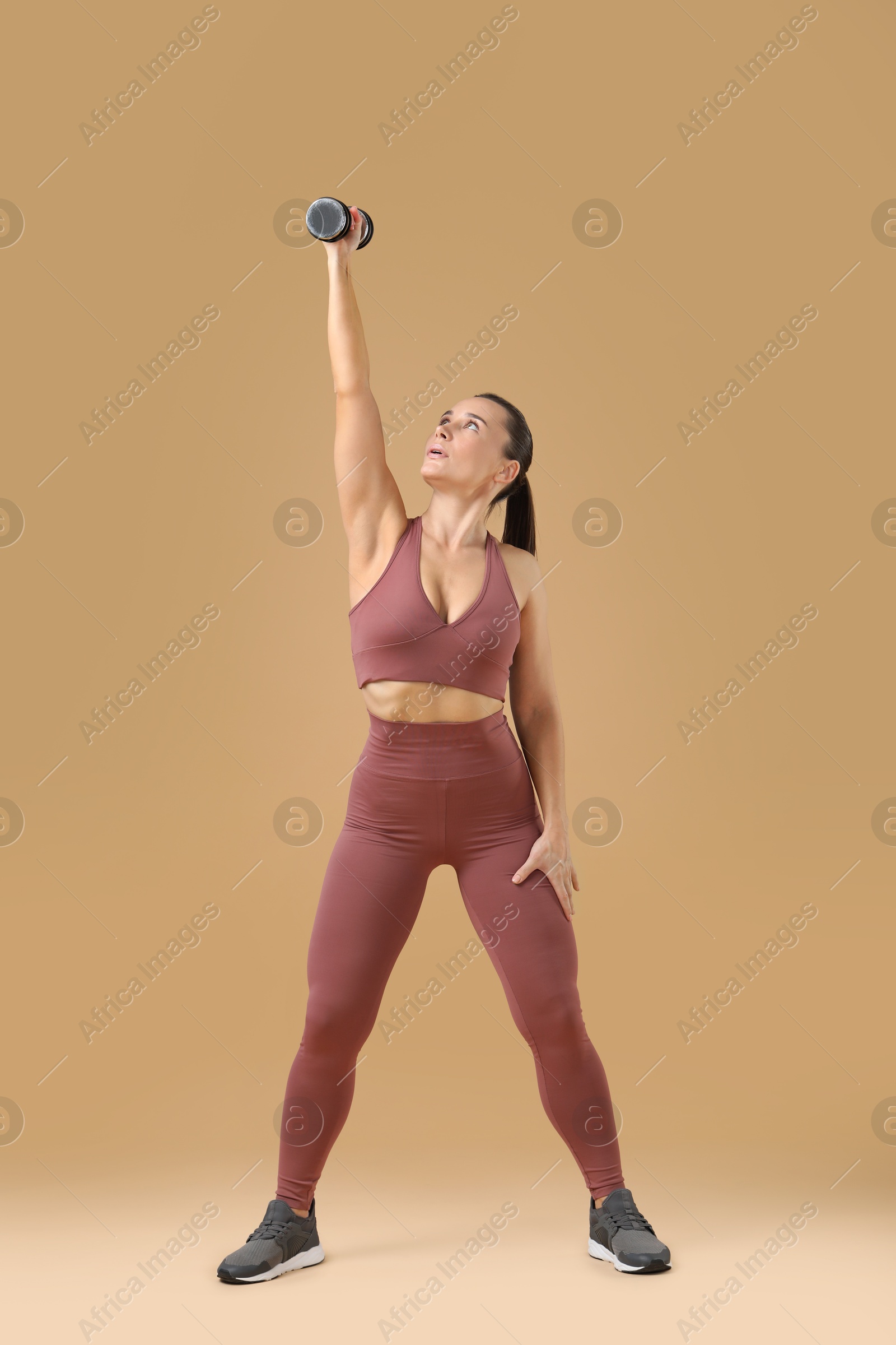 Photo of Woman exercising with dumbbell on beige background