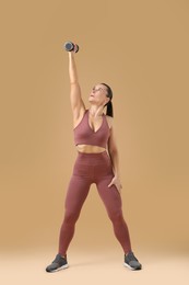 Photo of Woman exercising with dumbbell on beige background