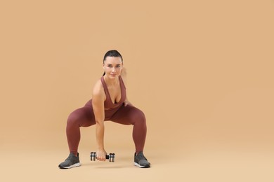 Photo of Woman exercising with dumbbell on beige background, space for text