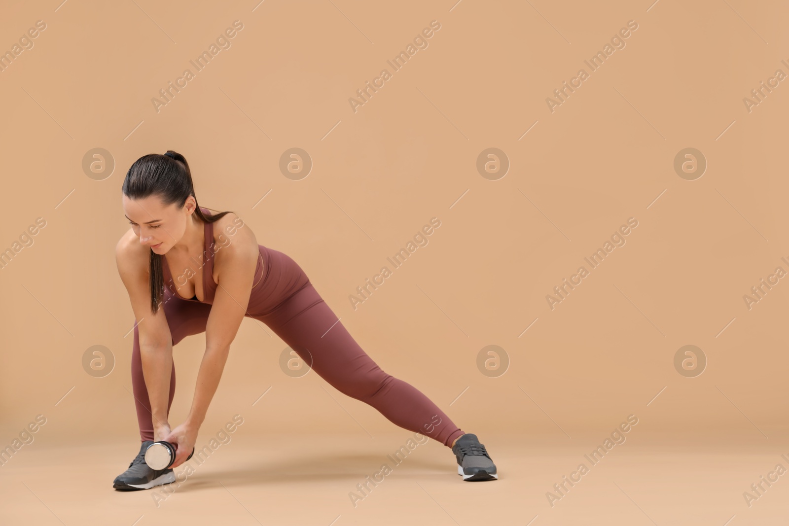 Photo of Woman exercising with dumbbell on beige background, space for text