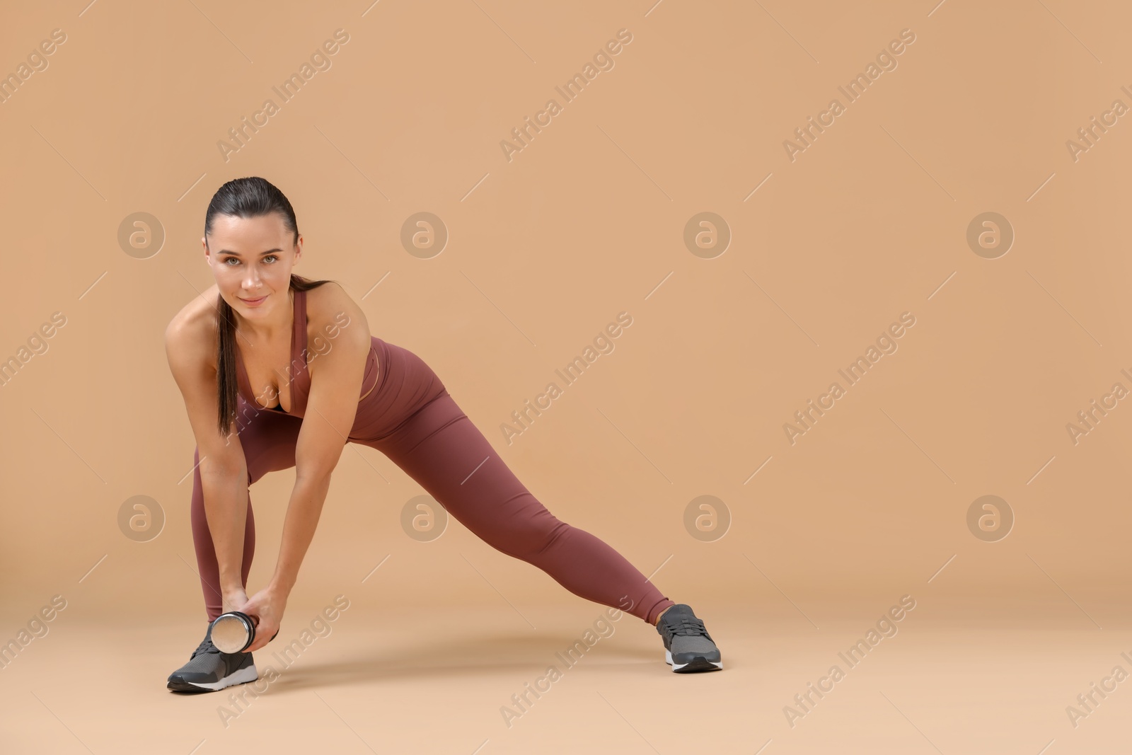 Photo of Woman exercising with dumbbell on beige background, space for text