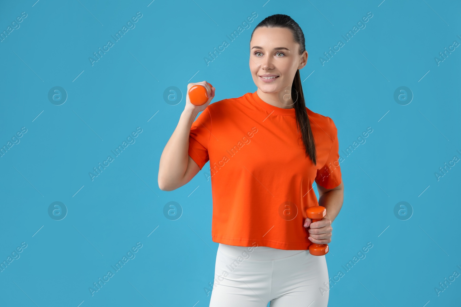 Photo of Woman exercising with dumbbells on light blue background, space for text