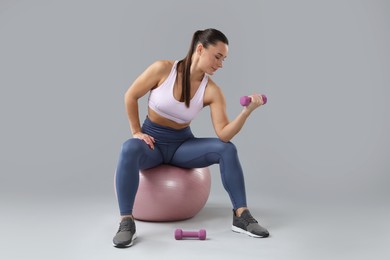 Photo of Woman exercising with dumbbells on fitball against light grey background