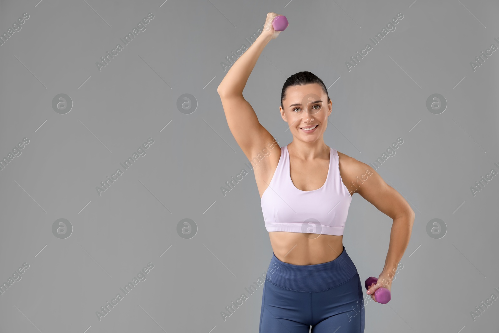 Photo of Woman exercising with dumbbells on light grey background, space for text