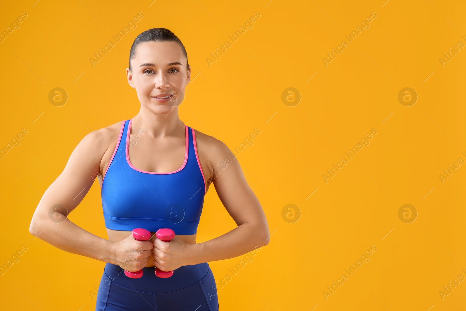 Photo of Woman exercising with dumbbells on orange background, space for text