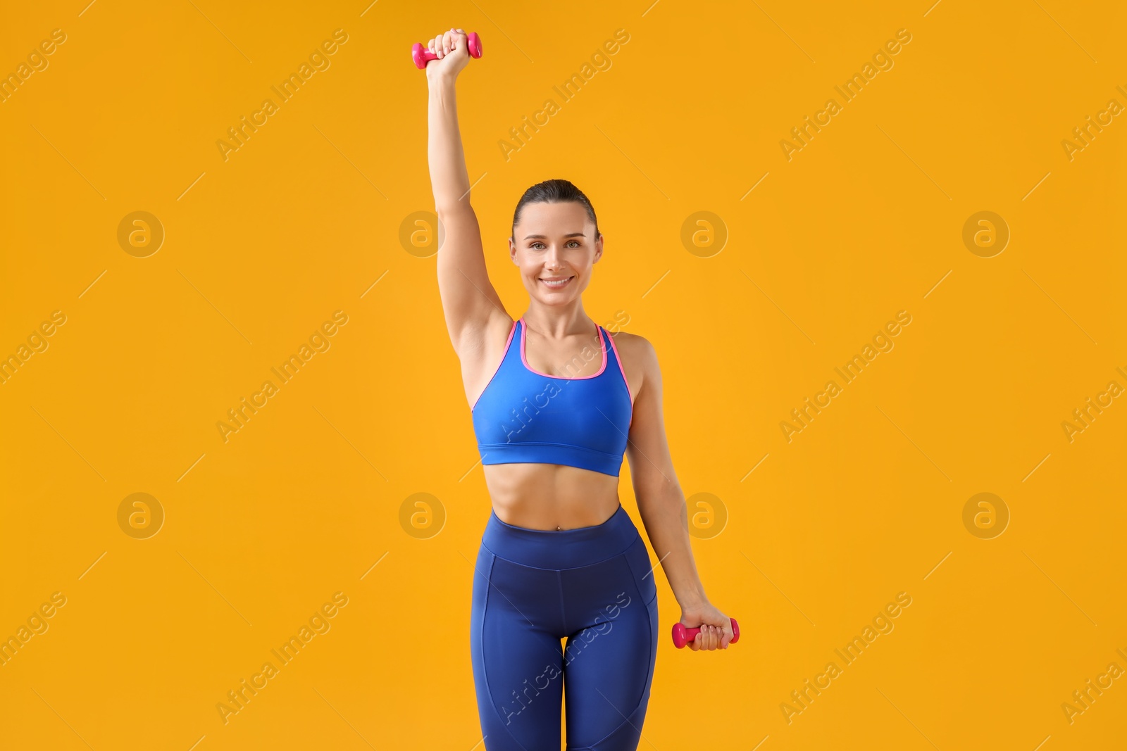 Photo of Woman exercising with dumbbells on orange background